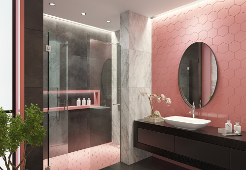 Luxurious bathroom with light pink honeycomb ceramic tiles and gray
and marble large ceramics

long black vanity unit with drawers on a wall with pink honeycomb shaped ceramics
black stone finish, two rectangular white ceramic washbasins, stainless steel 
vanity sink faucets and a blooming bonsai tree. 
walk-in shower with glass door, gray large ceramic tiles,decorating wall shelf 
with pink frame and pink honeycomb floor tiles.
ceiling with strip cove lighting and embedded spotlights.
