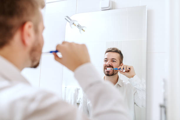 istock Businessman brushing his teeth while standing in front of mirror in bathroom. Morning routine concept. 1124557288