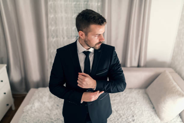 portrait of young businessman tying cufflinks on jacket and looking away. - haute couture beautiful smoking beauty imagens e fotografias de stock