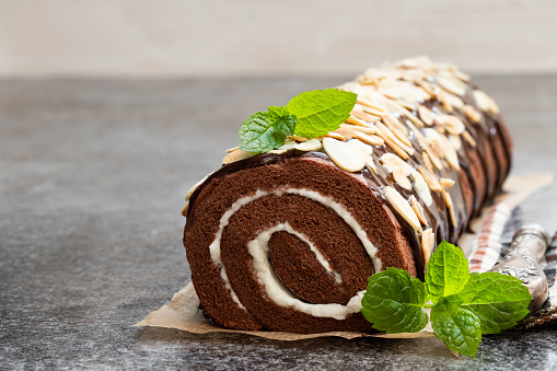 Chocolate  swiss roll with almond flakes on gray table