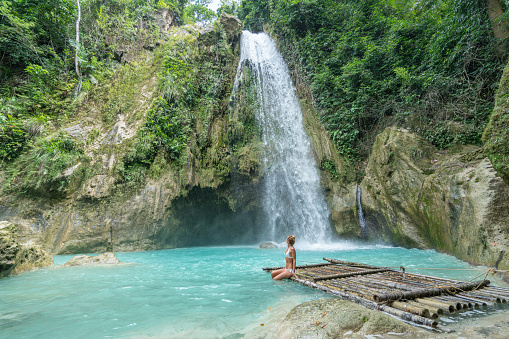 Young woman contemplating a beautiful waterfall on the Cebu Island in the Philippines. People travel nature loving concept. One person only enjoying outdoors and tranquillity in a peaceful environment