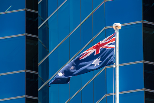 Flag of Australia waving in light breeze in front of modern skyscraper