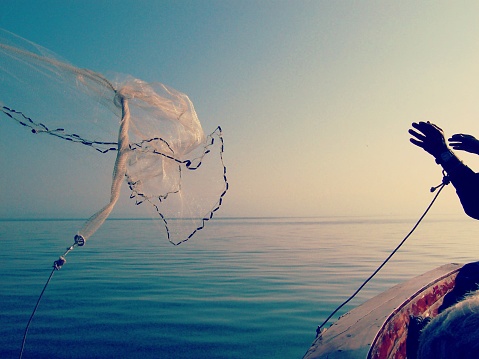 Man throwing Fishing net off boat and into the Sea Of Galilee Israel.