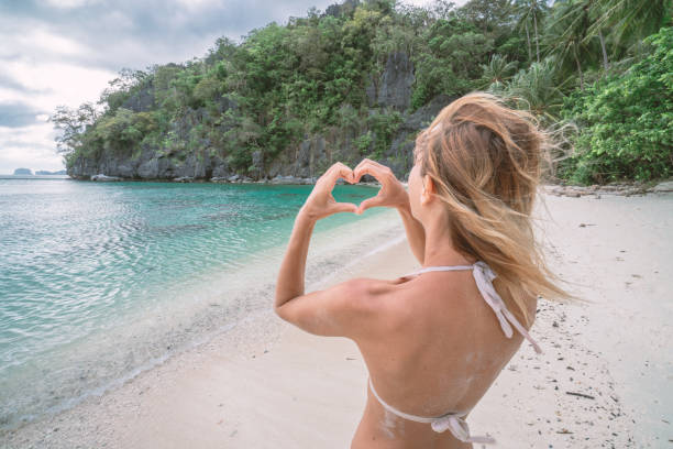 istock Young woman making heart shape finger frame on idyllic beach 1124580837