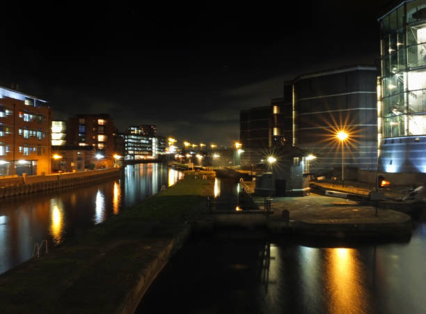 the lock entrance and moorings at canal side of clarence dock in leeds at night with buildings of the city reflected in the water and glowing street lights - leeds england yorkshire canal museum imagens e fotografias de stock