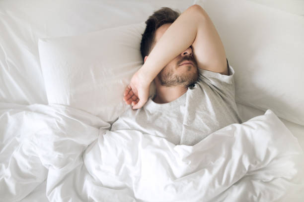 jeune homme fatigué dans le lit fermant ses yeux avant de se réveiller. le matin de la gueule de bois. troubles du sommeil et problèmes. - frustration male beauty one person problems photos et images de collection