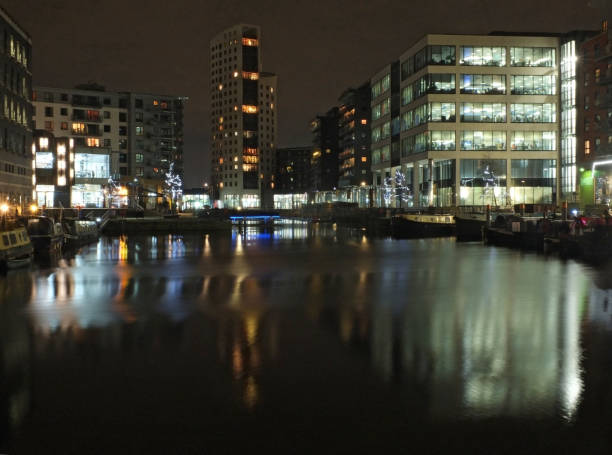 clarence dock in leeds at night with brightly illuminated buildings reflected in the water and boats moored along the sides - leeds england yorkshire canal museum imagens e fotografias de stock