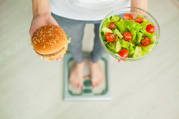 Dieting concept, beautiful young woman choosing between healthy food and junk food Dieting concept, beautiful young woman choosing between healthy food and junk food. low body fat stock pictures, royalty-free photos & images