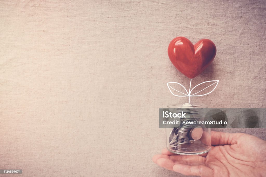 Hand holding a jar of heart tree growing on money coins, social responsibility and donation concept Charity and Relief Work Stock Photo