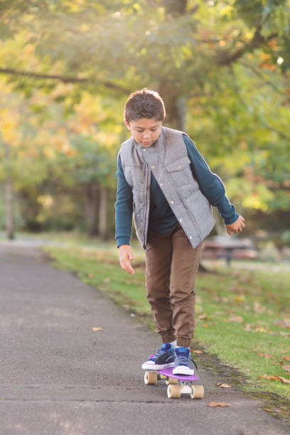 istock Elementary-age boy skates through a park on a penny board 1124603693