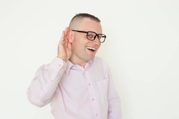 Joyful office worker in glasses overhearing Joyful office worker in glasses overhearing. Young man in stripped shirt listening to important news with hand at ear. Audio concept crew cut stock pictures, royalty-free photos & images