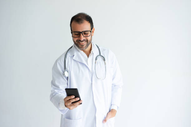 lächelnd gut aussehend männlichen arzt lesen nachrichten auf smartphone - doctor male doctor mature men portrait stock-fotos und bilder