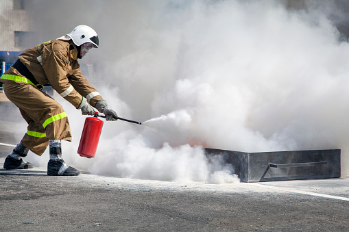 Extinguishing a major fire. A professional fireman in a special suit extinguishes an open fire with a fire extinguisher. Training firefighters for extinguishing fires