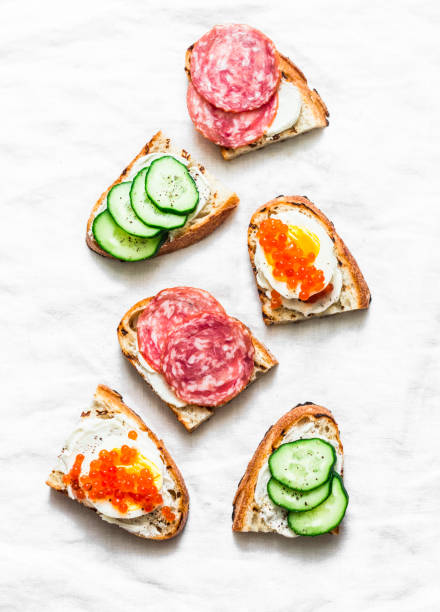 istock Appetizer sandwiches with red caviar, egg, sausage, cucumber and cream cheese on white background, top view 1124627385