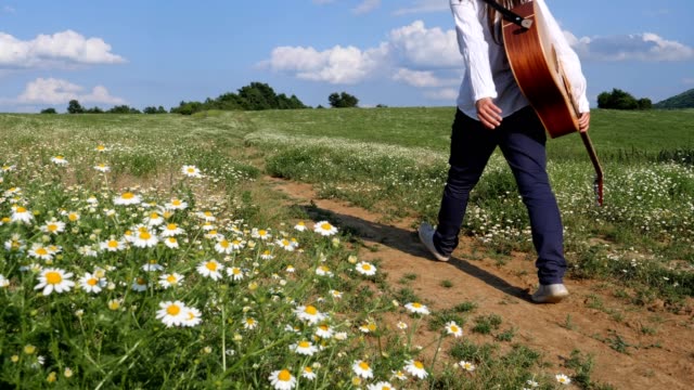 Slow motion of a young emancipated woman, a musician walking in the countryside on a rural road, hitchhiking, travelling only with her acoustic guitar, summer adventures