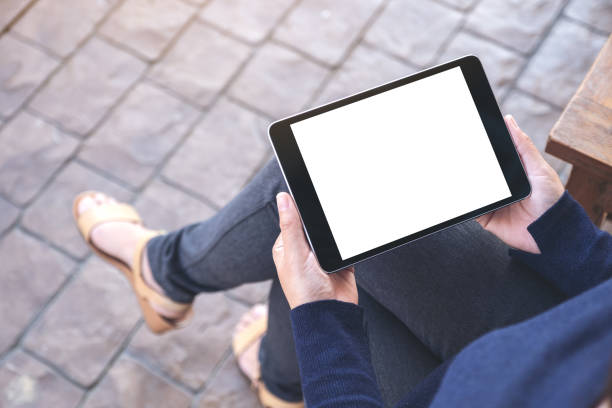 istock Mockup image of a woman holding black tablet pc with blank white screen horizontally while sitting in the outdoors 1124631808