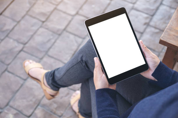 istock Mockup image of a woman holding black tablet pc with blank white screen while sitting in the outdoors 1124631827