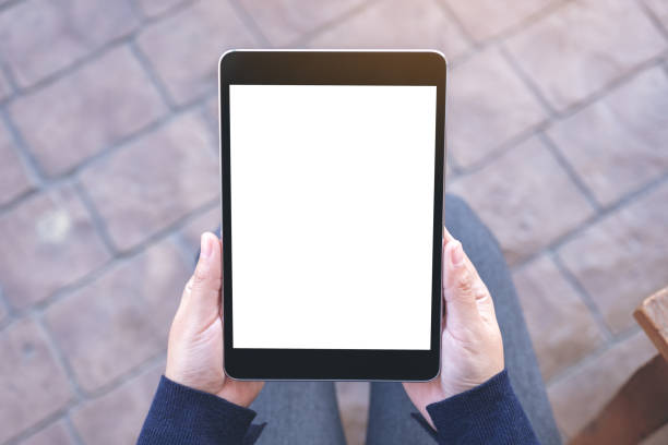 istock Top view mockup image of a woman holding black tablet pc with blank white screen while sitting in the outdoors 1124631833