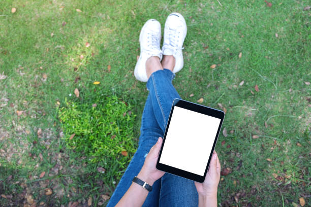 istock Top view mockup image of a woman holding and using black tablet pc with blank white desktop screen while sitting in the outdoors 1124631862