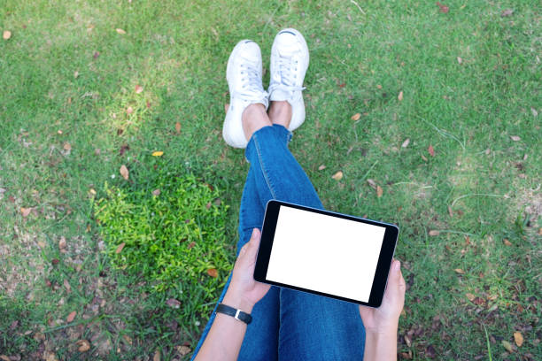 istock Top view mockup image of a woman holding and using black tablet pc with blank white desktop screen while sitting in the outdoors 1124631872