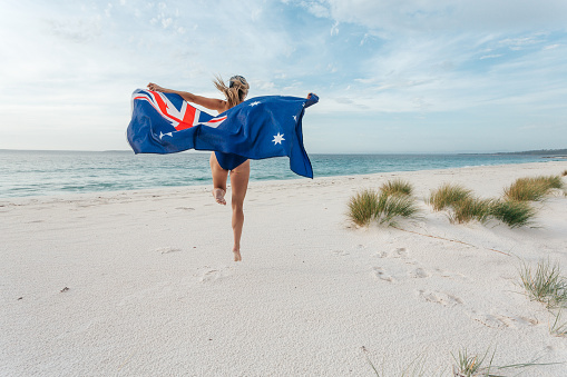 Jump for joy.  Woman leaping into the air with the Australian flag on a pretty beach.  Australian supporter, sports, fan, Australia Day celebrations