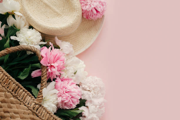 istock Straw hat and rustic bag with white and pink peonies on pastel pink paper, flat lay.  Hello spring image with copy space. Summer vacation concept. International Women's Day 1124635389