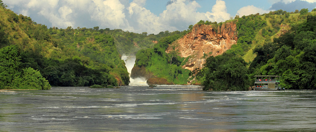 A panoramic shot of Murchison Falls with a river cruise boat and the surrounding river and jungle.