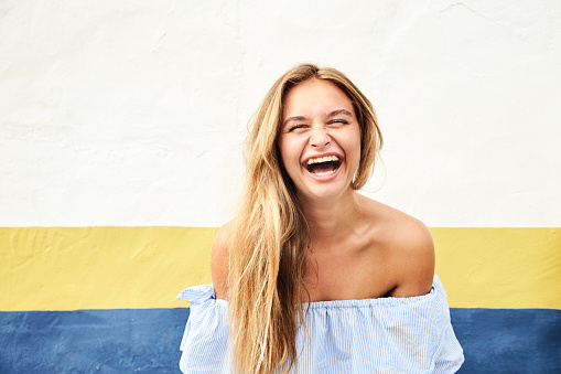 Laughing blond girl in front of wall, portrait