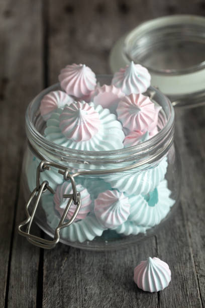 Light Pink and blue meringues in glass jar on dark background, vertical composition