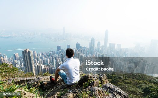 istock Men sitting on the top of mountain and looking cityscape 1124644013