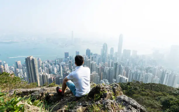 Photo of Men sitting on the top of mountain and looking cityscape