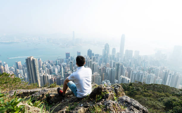 homens sentados no topo da montanha e olhando a paisagem urbana - men on top of climbing mountain - fotografias e filmes do acervo