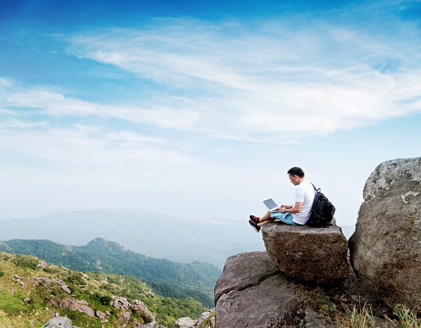 Man using laptop on top of mountain.