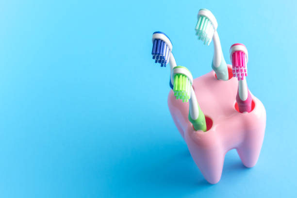 istock Colorful toothbrushes in a tooth-shaped pink container. Four toothbrushes in a tooth like container on blue. 1124646424
