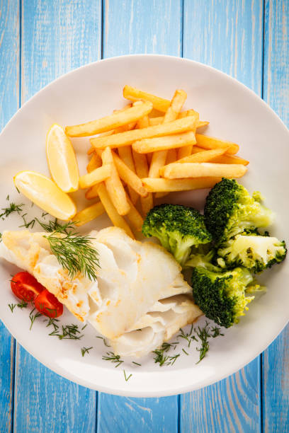 Fish dish - cod with French fries and vegetables on wooden background