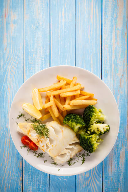 Fish dish - cod with French fries and vegetables on wooden background