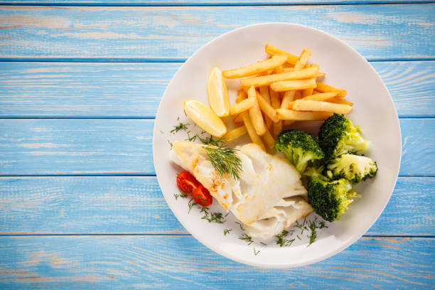 Fish dish - cod with French fries and vegetables on wooden background