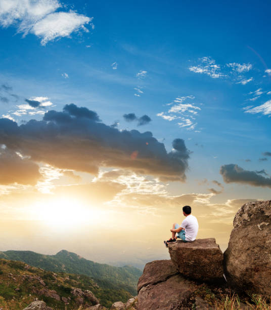 Man sitting on the top of mountain at sunset.