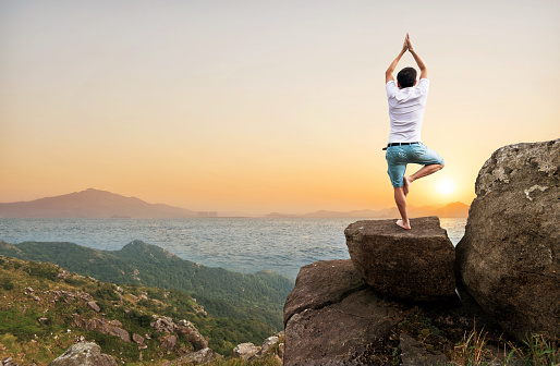 Man doing yoga on top of the cliff.