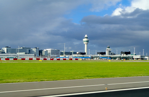 October 01st, 2018 : Amsterdam Schipol Airport, Amsterdam, Netherlands.  A view from an aircraft taking off at Amsterdam Schipol Airport.  The iconic air traffic control tower of Schipol seen amongst the terminal buildings.  In the foreground the grass and tarmac of the runway.