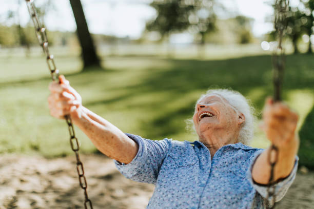 fröhliche senior frau auf einer schaukel auf einem spielplatz - swing stock-fotos und bilder