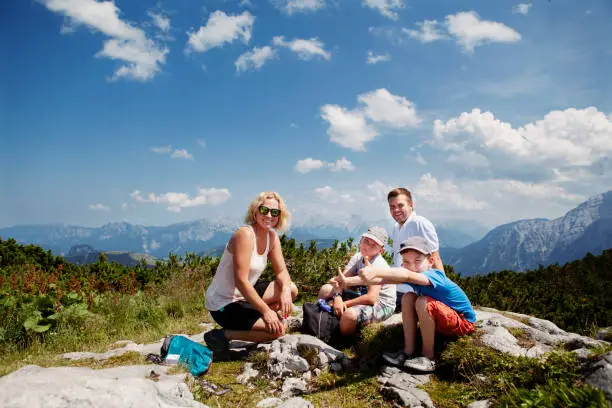 Two brothers and parents were hiking up the mountain on a hot summer day and enjoy a break stop and picnic