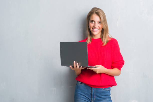 istock Beautiful young woman over grunge grey wall using computer laptop with a happy face standing and smiling with a confident smile showing teeth 1124664494