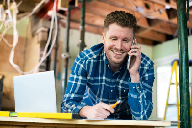 architekt wewnątrz domu jest odnowiony pracy na plany za pomocą laptopa i rozmowy na telefon komórkowy - indoors blueprint smiling built structure zdjęcia i obrazy z banku zdjęć