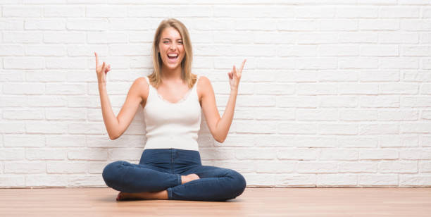 istock Beautiful young woman sitting on the floor at home shouting with crazy expression doing rock symbol with hands up. Music star. Heavy concept. 1124667174