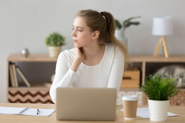 Photo of Serious woman looking away searching new ideas working on laptop