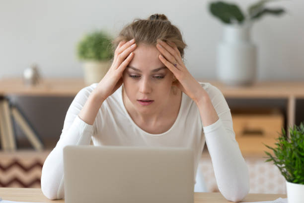 stressed young woman looking at laptop reading bad internet news - unemployment fear depression women imagens e fotografias de stock