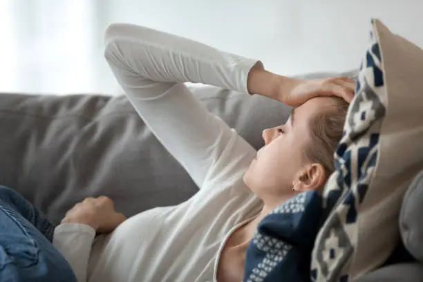 Photo of Upset depressed young woman lying on couch feeling strong headache