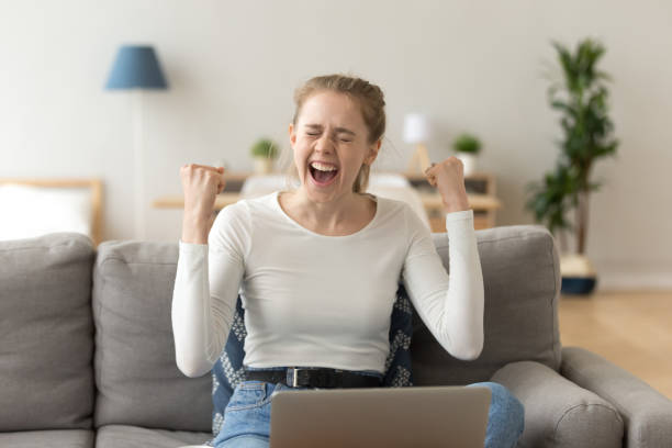 Happy girl celebrating victory excited by online win feeling winner Euphoric young woman celebrating victory excited by online win at home with laptop, happy girl student feeling successful got new job opportunity, received good exam test results feeling winner college acceptance letter stock pictures, royalty-free photos & images