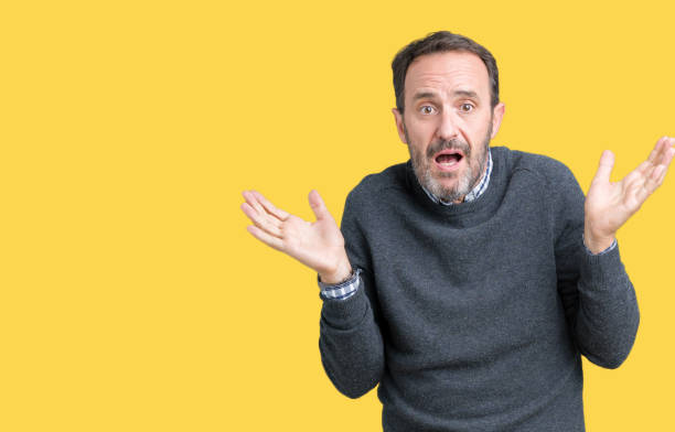 istock Handsome middle age senior man wearing a sweater over isolated background clueless and confused expression with arms and hands raised. Doubt concept. 1124668354